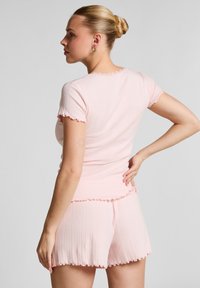 Roze geribde loungewear set met een t-shirt met korte mouwen en bijpassende shorts. Beide hebben gegolfde randen en een getailleerd ontwerp.