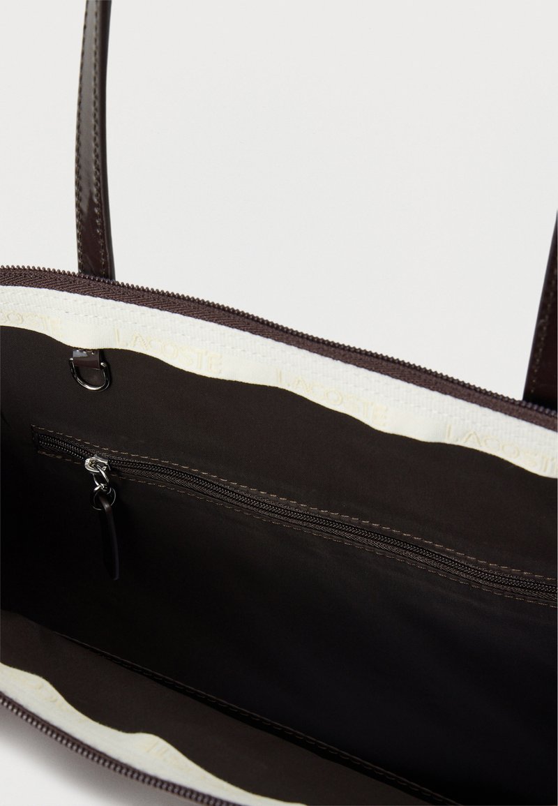 Inside view of dark brown handbag showing zippered pocket, fabric lining, and double leather handles extending upward.