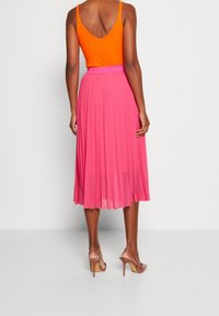 Top arancione senza maniche con scollatura a V, abbinato a una gonna plissettata rosa fino al ginocchio. Indossato con sandali nudi con tacco alto.