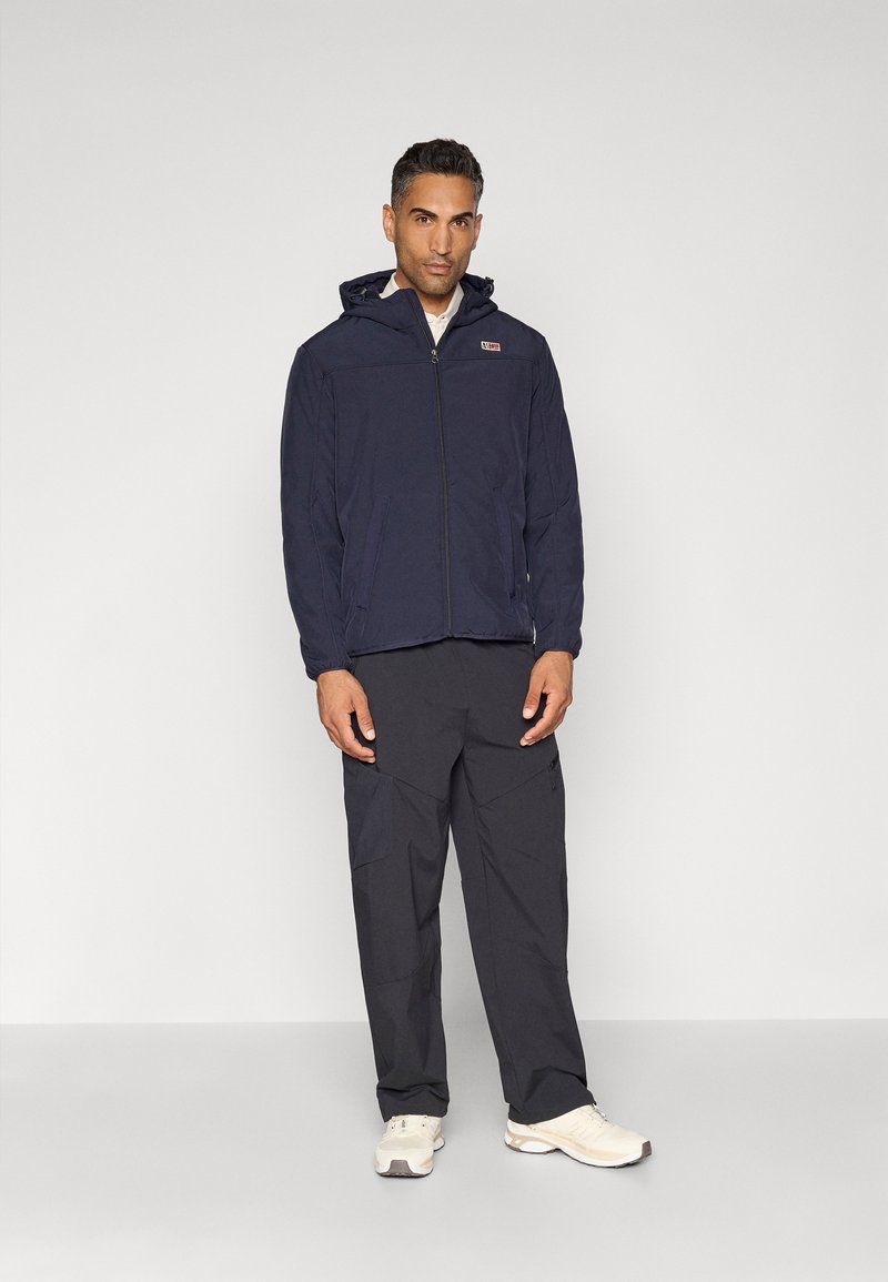 Chaqueta con capucha de color azul marino con cremallera, combinada con pantalones sueltos de color gris oscuro y zapatillas ligeras, con un logo en la chaqueta.