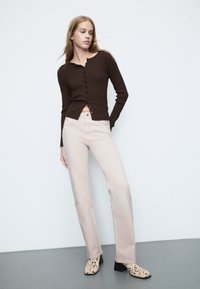 Brązowy sweter z prążkowanym wzorem i zapięciem na guziki, w połączeniu z jasnobeżowymi spodniami prostymi i wzorzystymi botkami na obcasie.