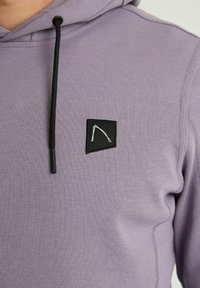 Haut à capuche violet en mélange de coton, arborant un patch rectangulaire noir avec un graphique blanc. Comprend des cordons de serrage noirs ajustables.