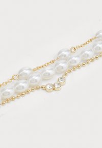Pulsera de perlas y oro que presenta perlas blancas lisas, acentos de cadena dorada y un trío de cristales transparentes redondos para un detalle adicional.