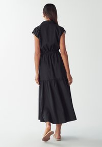 Mustaga lühikesed varrukad, kaelusekaelus, kokku tõmmatud vöökoht ja kihtidega seelik, valmistatud kergest kangast. Näha on paljaid jalgu sandaalides.