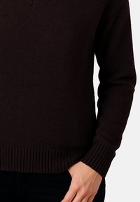 Tmavě hnědý pletený svetr s výstřihem do V, žebrovaným lemem a manžetami. Měkká textura, přiléhavý design a minimalistický vzhled.