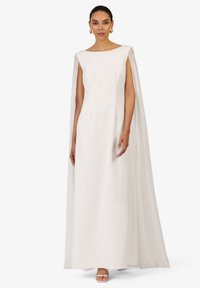 Robe blanche longue jusqu'au sol avec un décolleté en bateau et des manches cape attachées ; tissu lisse et design minimaliste ; accessoirisée avec des chaussures blanches.