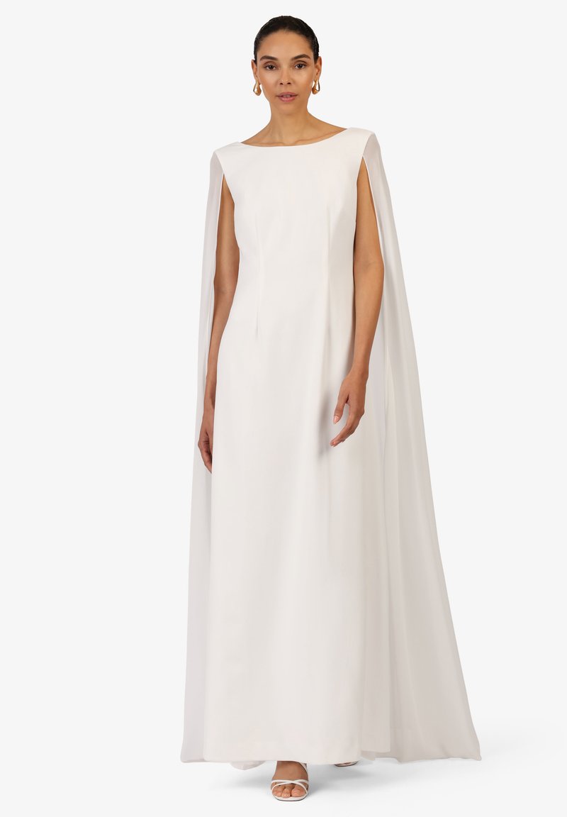 Hvid gulvlængde kjole med bådudskæring og påsyede kapesleeves; glat stof og minimalistisk design; accessoriseret med hvide sko.