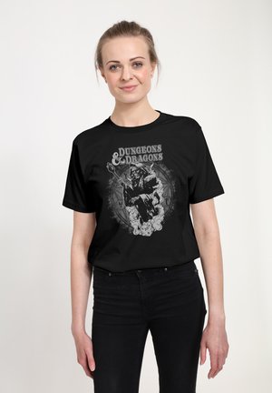 Mladá žena v černém tričku Dungeons & Dragons s motivem čaroděje, kostky d20 a mystických symbolů na bílém pozadí.