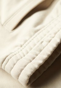 Tessuto beige con una morbida texture, caratterizzato da polsini arricciati e cuciture visibili, piegato ordinatamente, enfatizzando la sua superficie liscia e la forma.