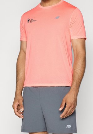 Mann trägt ein korallenfarbenes New Balance Kurzarmshirt mit dem New York City Marathon-Logo und graue New Balance Shorts.