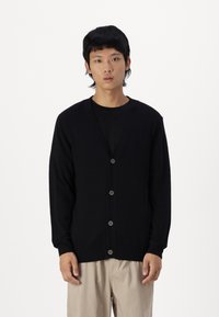 Svart cardigan laget av mykt stoff, med V-hals, lange ermer og seks frontknapper. Enkel design med ribbestrikkede mansjetter og nederkant.
