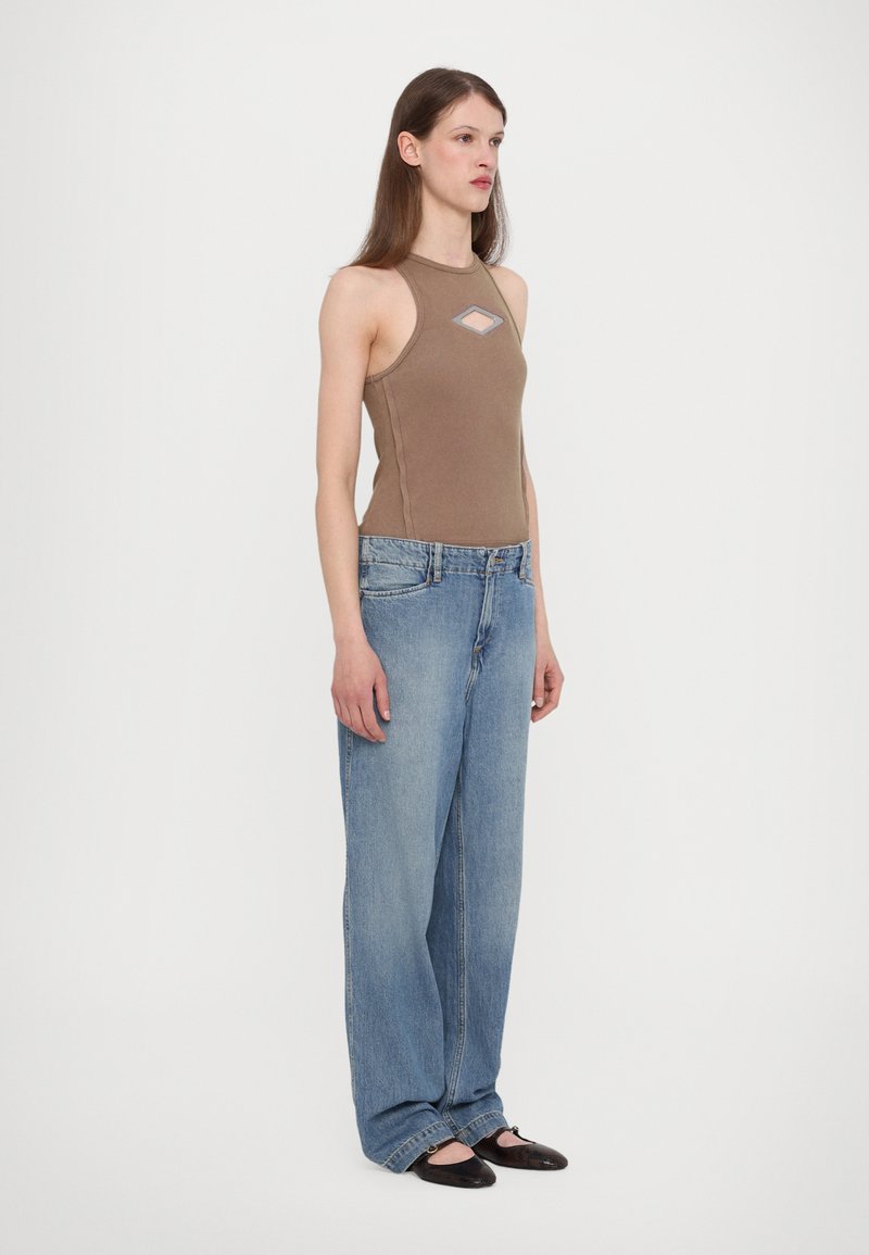 Braun ärmelloses Top mit einem Rautenausschnitt, kombiniert mit lockeren hellblauen Jeans und schwarzen Ballerinas, die einen lässigen Schnitt und weiche Texturen zeigen.