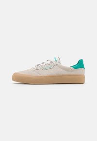 Beige suede sneaker with turquoise accents, featuring a textured gum sole and three side stripes. Laced with white flat shoelaces.