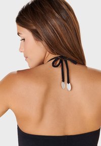 Mustat olkaimettomat yläosat, joissa on sileä pinta, ja takana oleva solmu, joka päättyy metallisiin yksityiskohtiin. Lähikuva yläselästä.