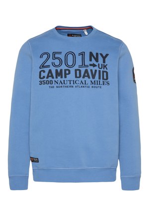 Sudadera azul claro con detalles en impresión negra. Presenta un cuello redondo, puños acanalados y un parche con el logo en la manga. Textura suave.