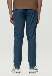Modré športové nohavice z ľahkého materiálu, s elastickým pásom a zužujúcimi sa nohavicami, v kombinácii s bielymi a tyrkysovými teniskami.