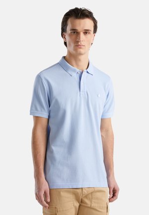 Polo shirt en coton bleu clair avec des manches courtes, texture douce et patte de boutonnage à trois boutons. Il présente un petit emblème sur la poitrine.