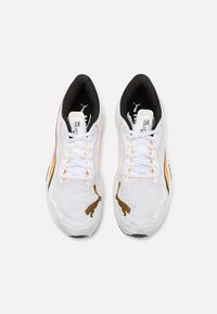 Zapatillas deportivas blancas con acentos en negro y naranja, parte superior de malla texturizada y detalles de logotipo prominentes en los lados y la lengüeta.