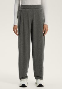 Grå löst sittande byxor i mjukt tyg, med hög midja och sidofållar, kombinerat med vita träningsskor.