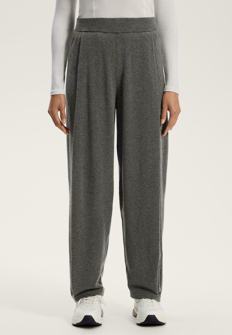 Grå löst sittande byxor i mjukt tyg, med hög midja och sidofållar, kombinerat med vita träningsskor.