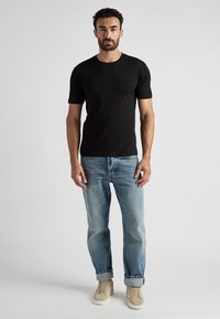 T-shirt noir à manches courtes associé à un jean bleu clair et des baskets beiges. La tenue présente une coupe classique et aucun motif visible.