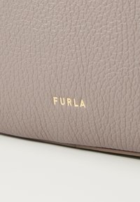 Vaaleanharmaa nahkalaukku, jossa on teksturoitu pinta. Koristeena kohopainettu kultainen brändinimi "FURLA". Kompakti suorakulmainen muoto minimalistisella muotoilulla.