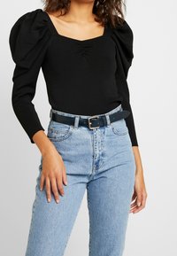 Zwarte lange mouwen bodysuit met poffende schouders en een vierkante halslijn, gecombineerd met lichtblauwe high-waisted jeans en een zwarte riem.