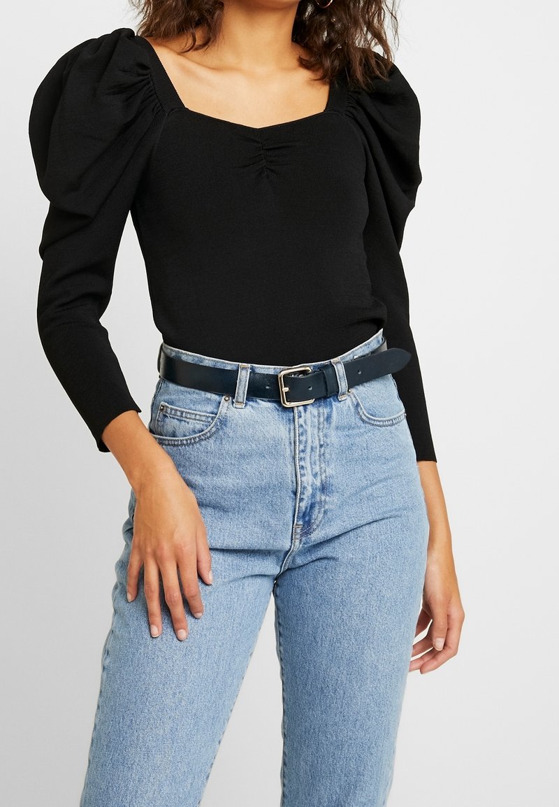 Zwarte lange mouwen bodysuit met poffende schouders en een vierkante halslijn, gecombineerd met lichtblauwe high-waisted jeans en een zwarte riem.
