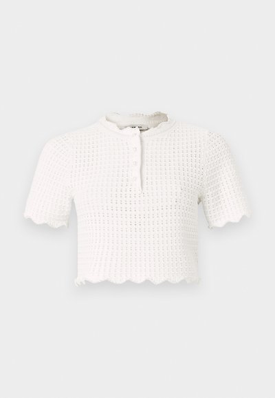 Hvit kortermet cropped topp med teksturert mønster, bølgekant og knappestenging, med rund hals og lett stoff.