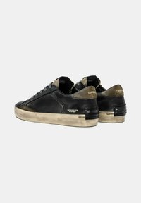 Un paio di sneakers nere basse con suole beige consumate e dettagli in suede verde oliva, che mostrano la frase "Distressed with No Stress" sui lati.