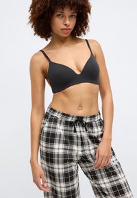 Bralette de algodão preto com design em V e alças finas, combinado com calças de pijama xadrez em preto e branco com uma cintura elástica.