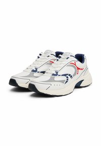 Sneakers atletici bianchi con accenti blu navy e rossi, dotati di pannelli in rete, suole spesse e una finitura texturizzata sulla parte superiore e sui lati.