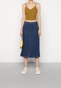 Kermanneuletyylinen lyhyt yläosa, tummansinisestä denimmateriaalista valmistettu midi-hame, jossa on edessä halkio, valkoiset platform-kengät ja pieni keltainen käsilaukku.