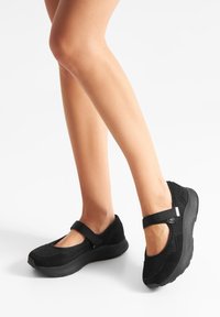 Zapatos de malla negra con un diseño tipo Mary Jane, acentos de ante suave, punta redondeada y suela acolchada para mayor comodidad. Incluye correa ajustable.