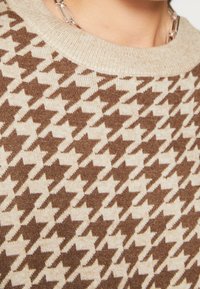 Stickad tröja med ett hundtandmönster i brunt och kräm, med en krämfärgad ribbad rundad halsringning och mjuk textur.