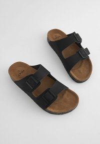 Sandali neri slip-on con due cinturini regolabili e fibbie, dotati di una soletta in suede marrone e una suola testurizzata con accenti in sughero.
