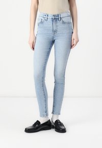 Jeans ajustados de talle alto en azul claro con una textura suave, que cuentan con cinco bolsillos y pasadores para cinturón, combinados con mocasines negros.