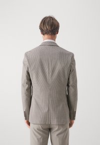 Szary żakiet w wzór houndstooth z wyłogami, pojedynczym rozcięciem i brązowymi guzikami jako akcentami. Dopasowany krój noszony na jasnych spodniach.