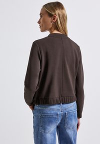 Brun pulloverjacka med ribbat nederkant, rund hals och långa ärmar. Bärs med ljusblå denimjeans. Slät textur, minimalistisk design.