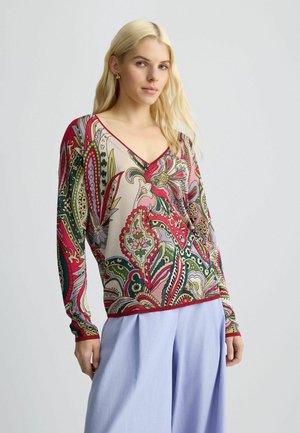 V-neck patterned sweater in cream, featuring intricate floral and paisley designs in red, green, and pink. Long sleeves with red trim.