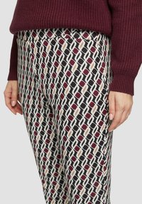 Pantalons à motif avec un design géométrique en bordeaux, crème et noir. Tissu doux avec une texture lisse et une taille élastique.