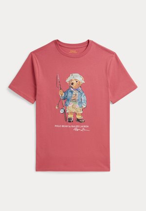 Czerwona koszulka z krótkim rękawem z niedźwiedziem ubranym w strój wędkarski trzymającym wędkę, z napisem „Polo Bear by Ralph Lauren” poniżej.