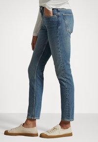 Ljusblå denimjeans med slim fit, med fem fickor, knappstängning och subtila blekningar. Kombineras med beiga sneakers i canvas.