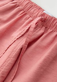 Pantalon avec taille élastique rose corail, cordon noué et surpiqûres détaillées le long de la couture avant.