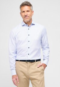 Helles blaues Langarmhemd mit einem subtilen Muster, Button-Down-Kragen und dunklen Knöpfen, kombiniert mit khakifarbenen Hosen und einem schwarzen Gürtel.