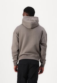 Gray hoodie with a relaxed fit, featuring a large hood and ribbed cuffs. Worn with black cargo pants, showing a simple, casual design.