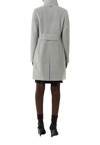Helle graue Wolljacke mit hohem Kragen, Rückengeschnürung und sauberer Nahtverarbeitung. Mid-Length-Design mit einer klaren, schlanken Form und ohne sichtbare Muster.