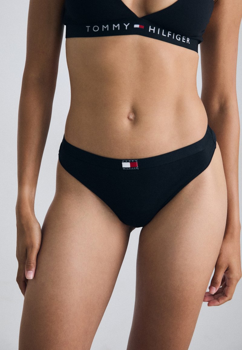 Culottes de bikini en coton noir avec une texture lisse, présentant un accent logo Tommy Hilfiger blanc et rouge sur la taille.