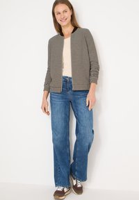 Veste bomber ray ée avec un col sombre, portée sur un haut clair et un jean bleu à jambes larges ; associée à des baskets marron avec des accents blancs.