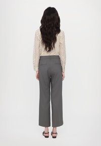 Gray tailored trousers with a straight leg and back pockets, paired with a cream blouse featuring a subtle floral print.